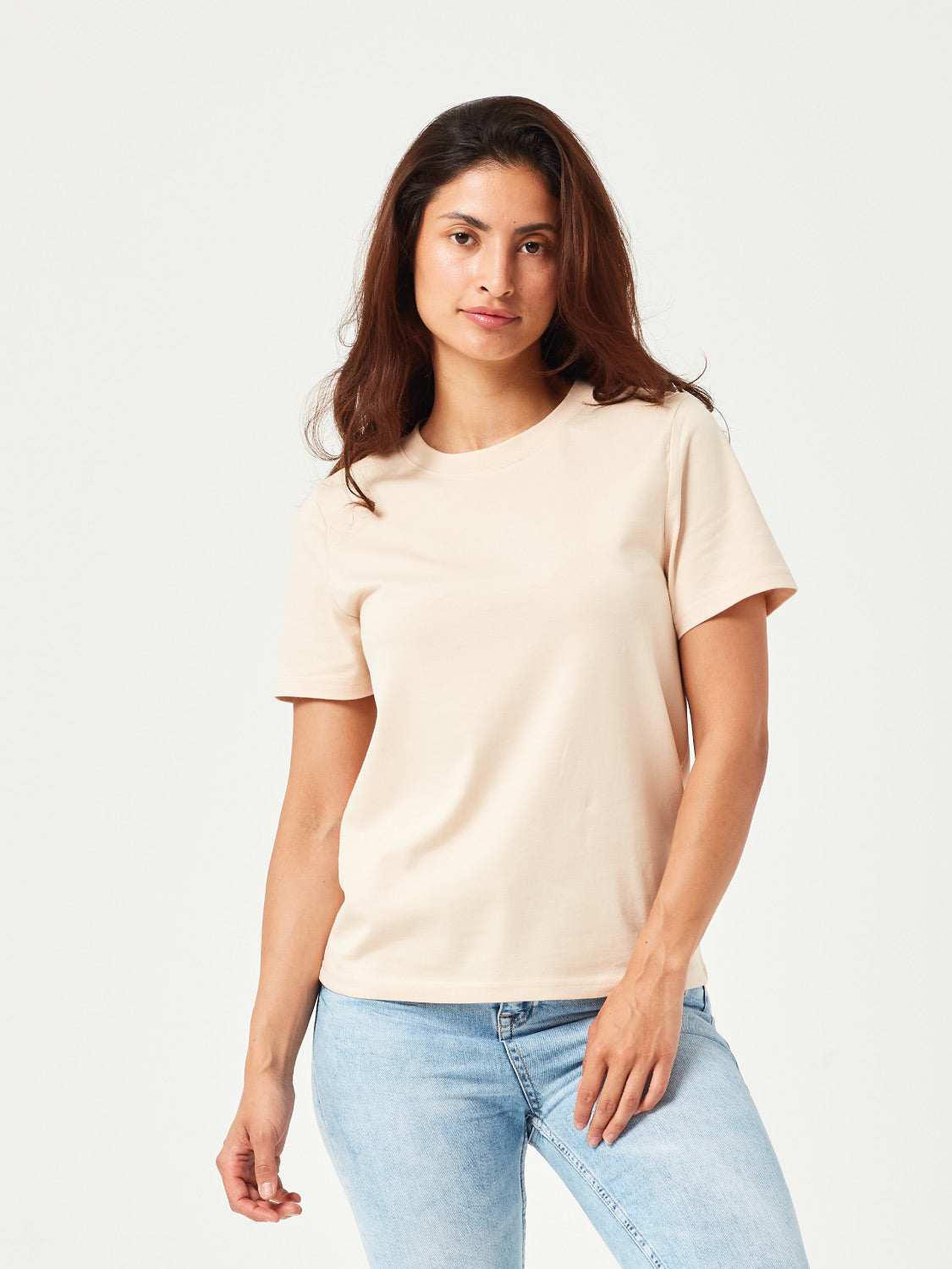 Frau in sand farbenen T-Shirt und hellblauen zerrissenen Jeans, steht mit dem Rücken zur Kamera, weinrote Sneakers, vor weißem Hintergrund.