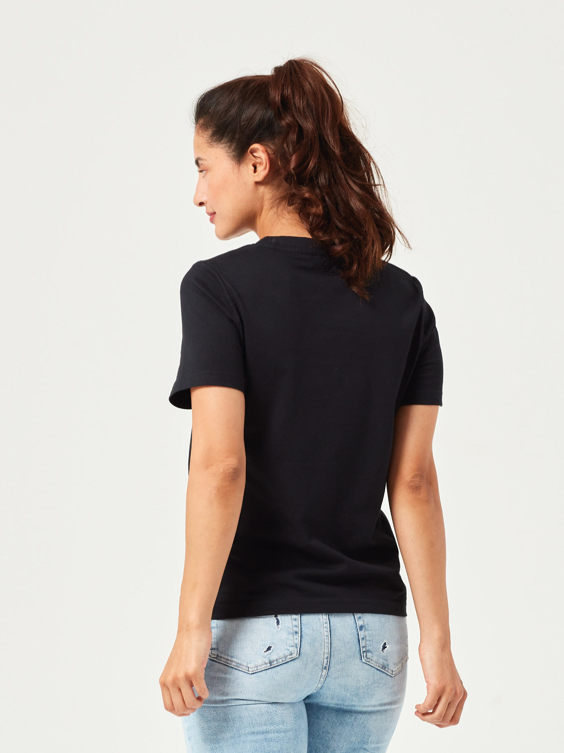 Rückenansicht eines schwarzen Damen T-Shirts aus Bio-Baumwolle, getragen von Frau mit lockigem Haar. Schlichtes, komfortables Basic-Shirt mit Rundhalsausschnitt und kurzen Ärmeln. Ideales Shirt für lässige Alltagslooks und umweltfreundliche Mode.