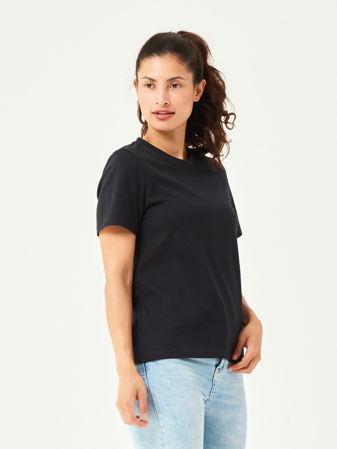 Schwarzes Damen T-Shirt aus hochwertiger Bio-Baumwolle, seitlich getragen von Frau mit hellblauer Jeans. Komfortables Rundhals-Shirt mit kurzen Ärmeln. Perfektes Basic für moderne Casual Styles und nachhaltige Damenmode