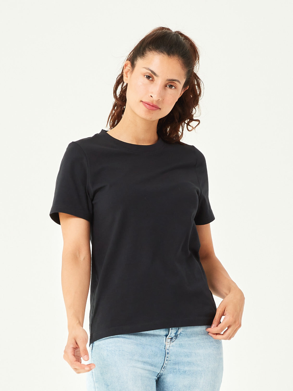 Frau trägt ein schwarzes Damen T-Shirt aus Bio-Baumwolle mit Rundhalsausschnitt und kurzen Ärmeln. Klassisches Basic-Shirt kombiniert mit hellblauer Jeans. Nachhaltige Mode für Casual Outfits, Freizeitlooks und Streetwear.