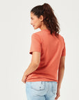 Frau trägt ein lässiges, orangefarbenes Damen T-Shirt aus nachhaltiger Bio-Baumwolle mit Rundhalsausschnitt und kurzen Ärmeln. Modisches Basic-Shirt kombiniert mit hellblauer Jeans. Nachhaltige Damenmode für Alltag, Freizeit und Streetwear. Bequemes und stilvolles T-Shirt für moderne Casual Outfits
