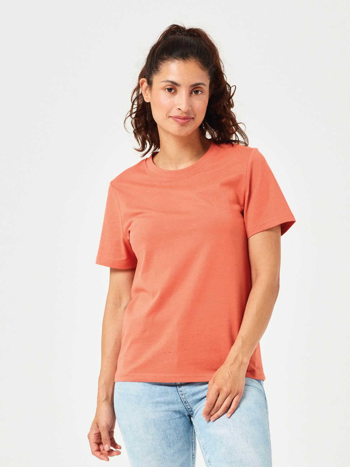 Frau trägt ein lässiges, orangefarbenes Damen T-Shirt aus nachhaltiger Bio-Baumwolle mit Rundhalsausschnitt und kurzen Ärmeln. Modisches Basic-Shirt kombiniert mit hellblauer Jeans. Nachhaltige Damenmode für Alltag, Freizeit und Streetwear. Bequemes und stilvolles T-Shirt für moderne Casual Outfits