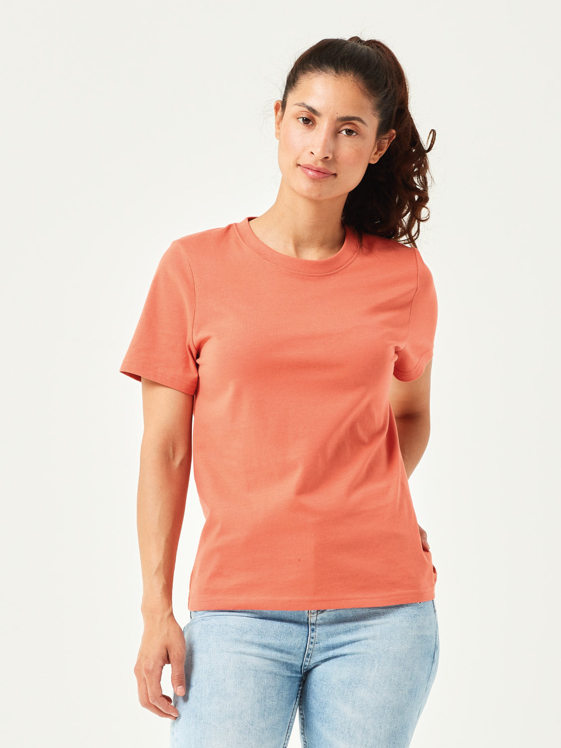 Frau in modernem, orangefarbenen T-Shirt aus hochwertiger Bio-Baumwolle. Kurzärmliges Basic-Shirt mit Rundhalsausschnitt, kombiniert mit hellblauer Jeans. Stilvolle, nachhaltige Damenmode für Alltag und Freizeitoutfits.
