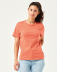 Frau in modernem, orangefarbenen T-Shirt aus hochwertiger Bio-Baumwolle. Kurzärmliges Basic-Shirt mit Rundhalsausschnitt, kombiniert mit hellblauer Jeans. Stilvolle, nachhaltige Damenmode für Alltag und Freizeitoutfits.