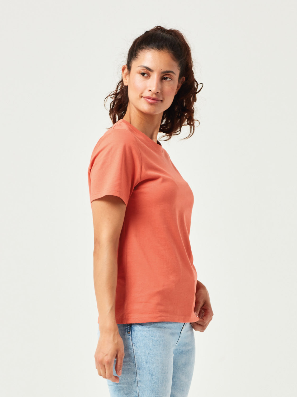 Frau in modernem, orangefarbenen T-Shirt aus hochwertiger Bio-Baumwolle. Kurzärmliges Basic-Shirt mit Rundhalsausschnitt, kombiniert mit hellblauer Jeans. Stilvolle, nachhaltige Damenmode für Alltag und Freizeitoutfits.