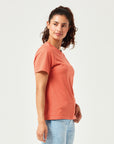 Frau in modernem, orangefarbenen T-Shirt aus hochwertiger Bio-Baumwolle. Kurzärmliges Basic-Shirt mit Rundhalsausschnitt, kombiniert mit hellblauer Jeans. Stilvolle, nachhaltige Damenmode für Alltag und Freizeitoutfits.