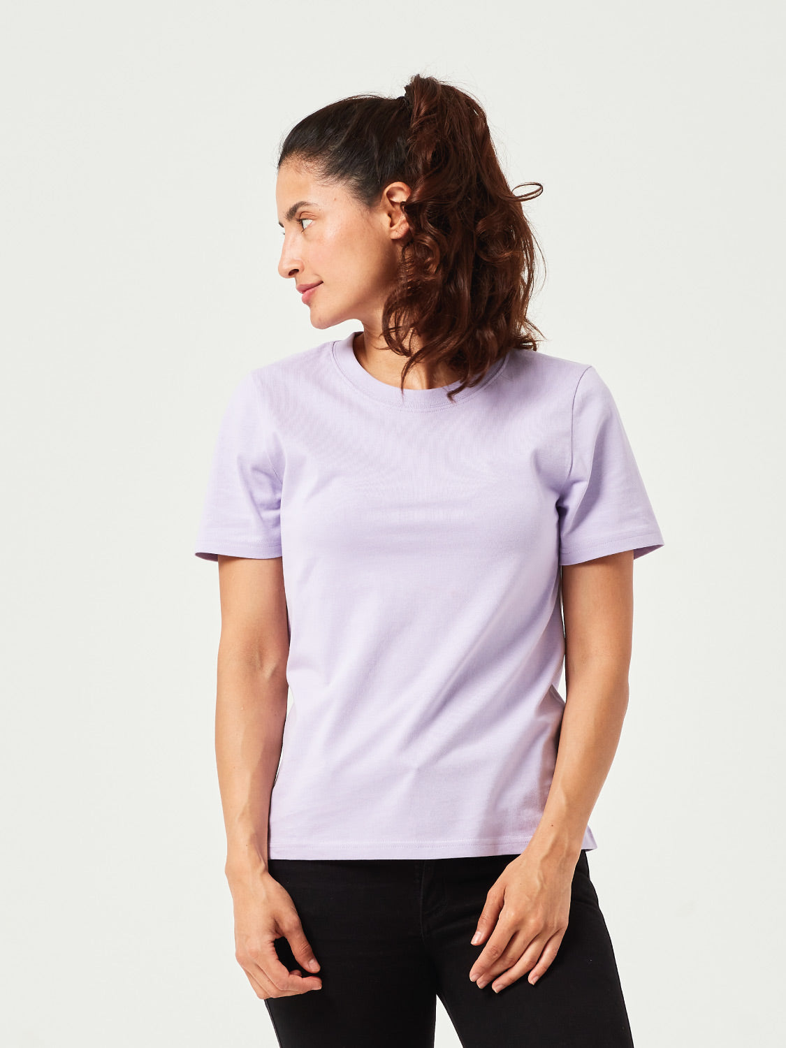 Frau in modernem, lila T-Shirt aus Bio-Baumwolle. Kurzärmliges Basic-Shirt mit Rundhalsausschnitt, kombiniert mit schwarzer Jeans. Perfekt für lässige Freizeitlooks und nachhaltige Mode.