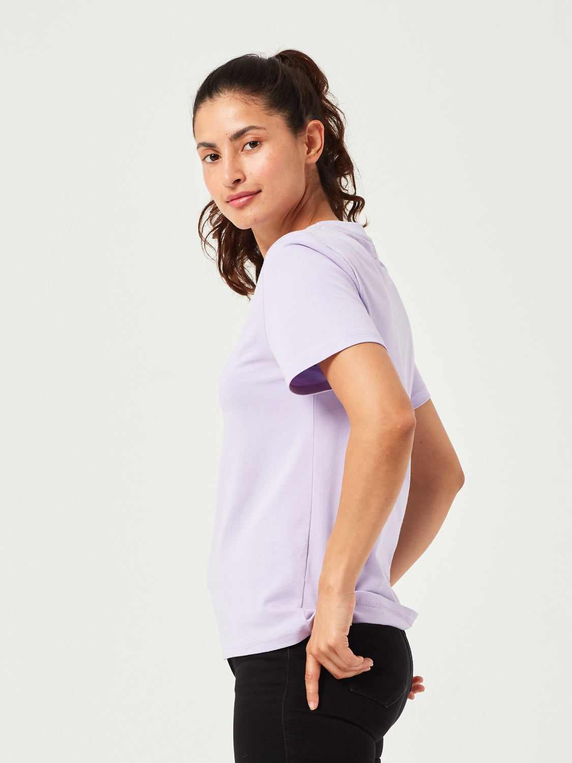 Lila Damen T-Shirt aus hochwertiger Bio-Baumwolle, getragen von Frau mit lockigem Haar. Komfortables Basic-Shirt mit Rundhalsausschnitt, perfekt kombiniert mit schwarzer Jeans. Moderne und nachhaltige Damenmode für lässige Outfits.