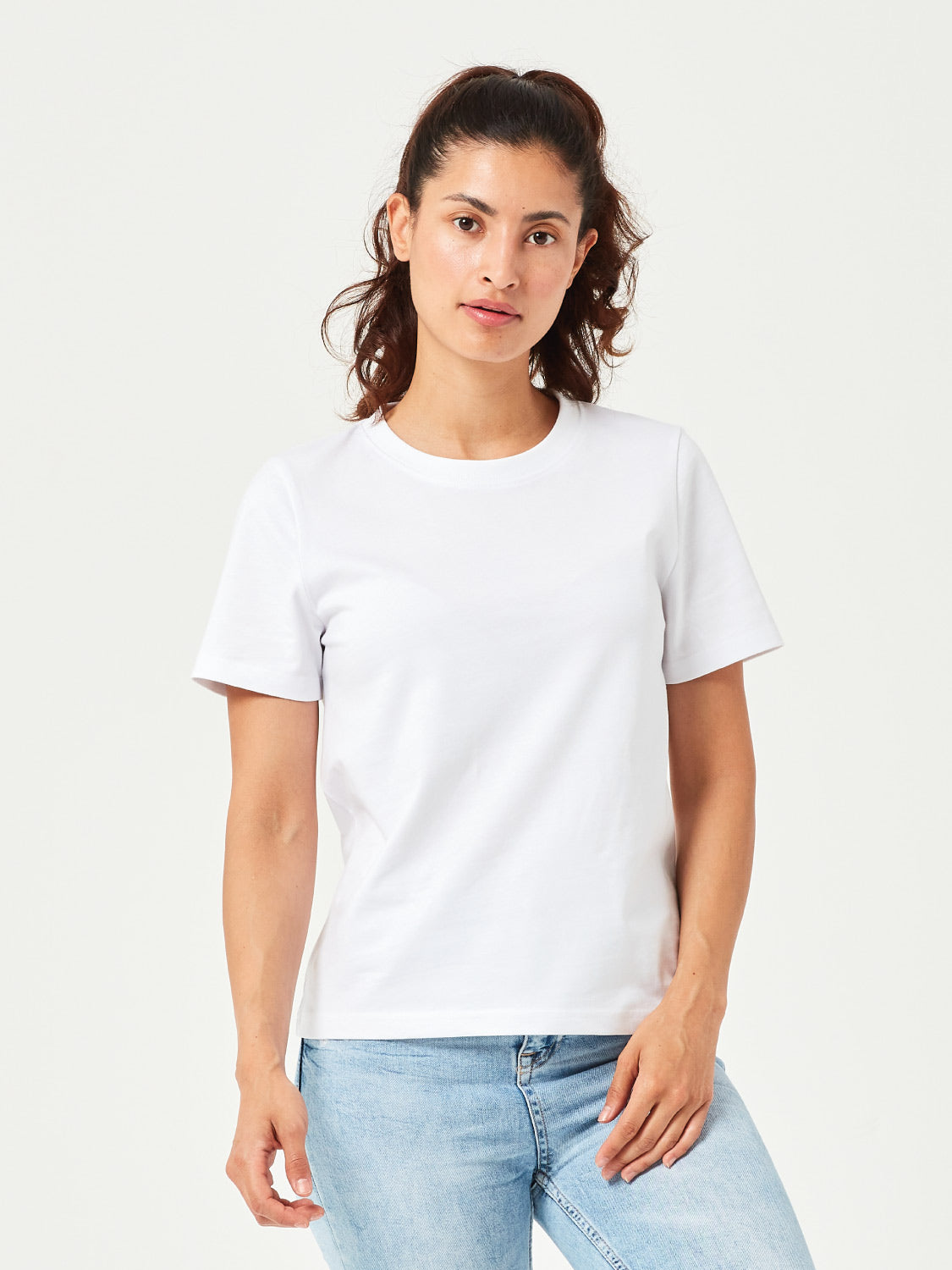 Frau trägt ein minimalistisches weisses Damen T-Shirt aus nachhaltiger Bio-Baumwolle. Komfortables Basic-Shirt mit Rundhalsausschnitt, perfekt kombiniert mit hellblauer Jeans. Ideal für Freizeit, Casual Outfits und moderne Streetwear.