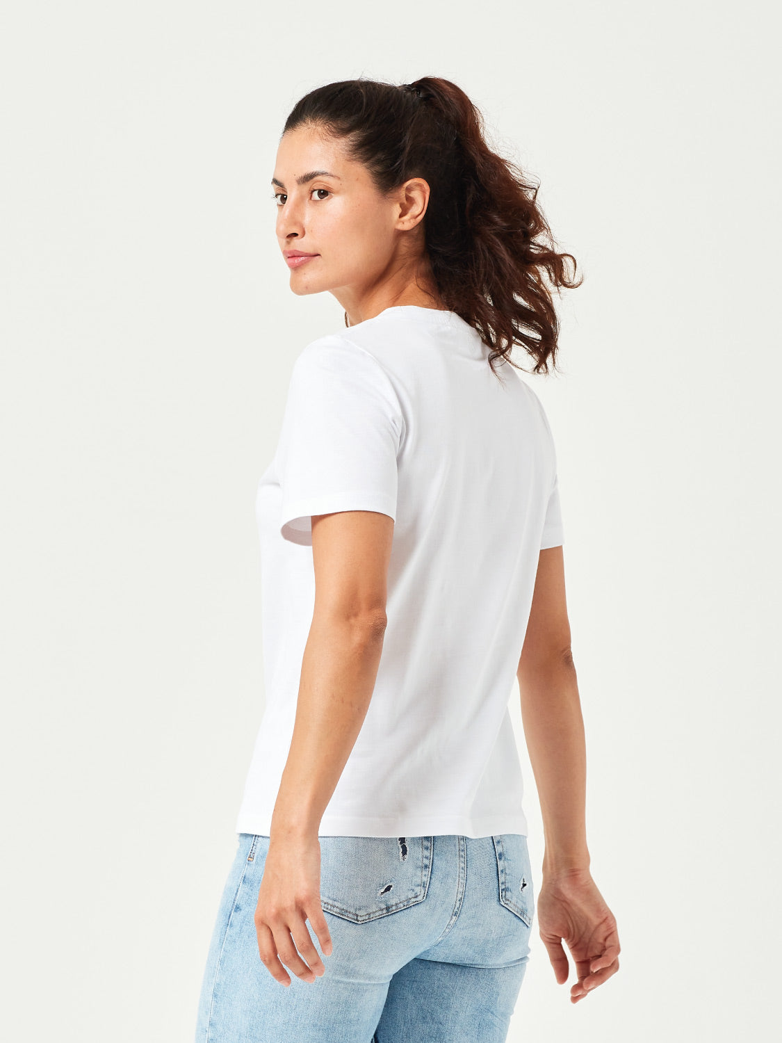 Weißes Damen T-Shirt aus hochwertiger Bio-Baumwolle, seitlich getragen von Frau mit hellblauer Jeans. Komfortables Rundhals-Shirt mit kurzen Ärmeln. Perfektes Basic für moderne Casual Styles und nachhaltige Damenmode.