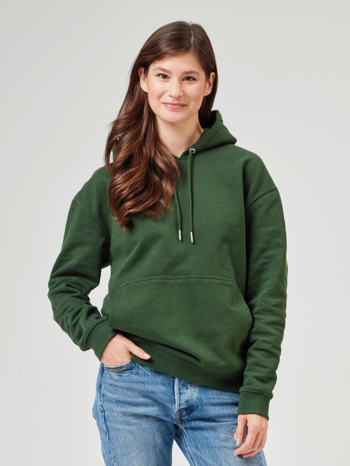 Unisex Hoodie in Dunkelgrün aus Bio-Baumwolle mit Kapuze und Kängurutasche. Lässiger Kapuzenpullover kombiniert mit blauer Jeans. Nachhaltige Mode für Männer und Frauen, perfekt für Freizeitlooks und Streetwear.