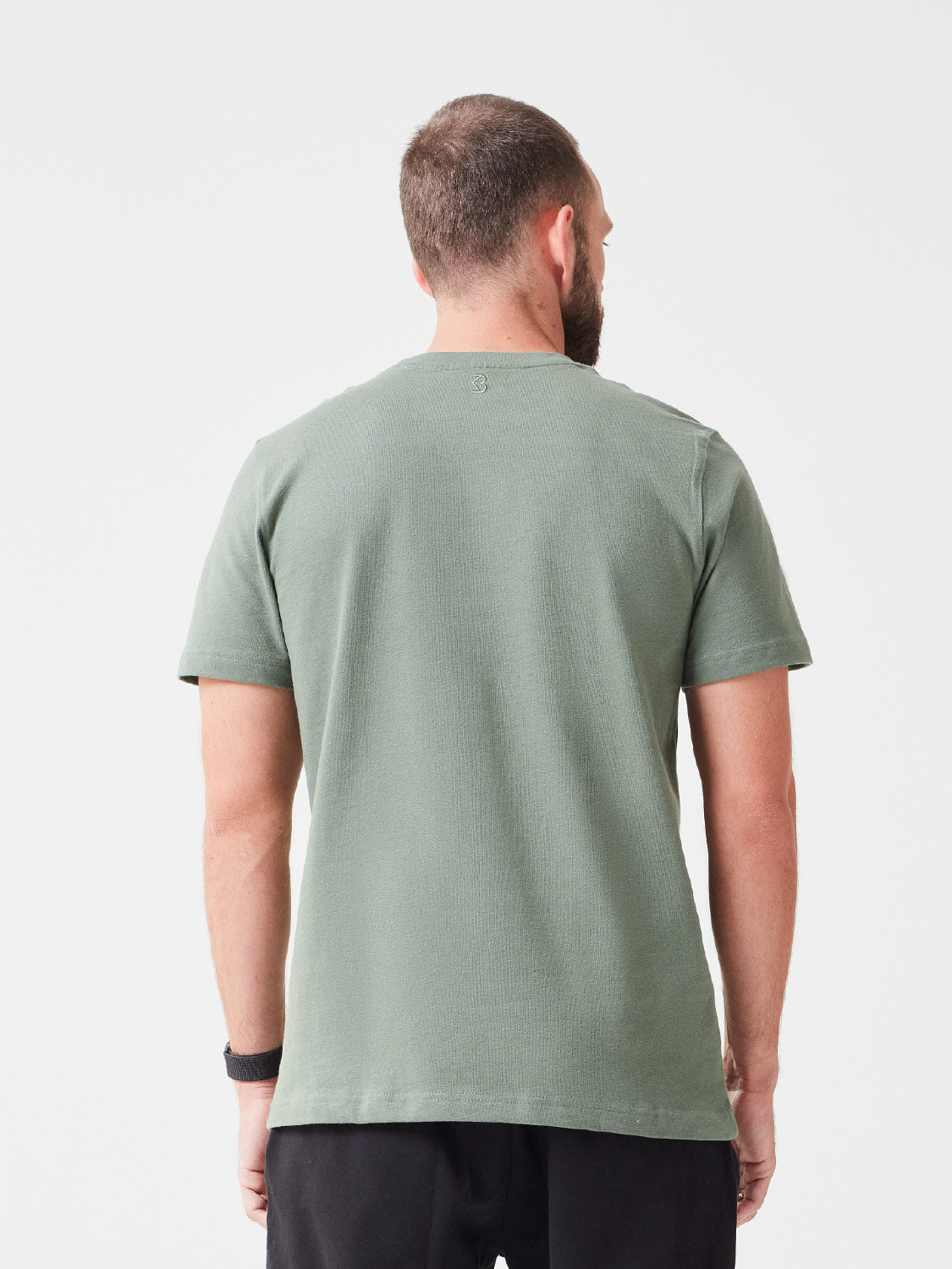 Rückansicht eines Mannes der ein Premium TShirt in der Farbe Grün aus Bio-Baumwolle trägt, dazu hat er eine passende schwarze Hose an - nachhaltige Mode für einen lässigen Look.