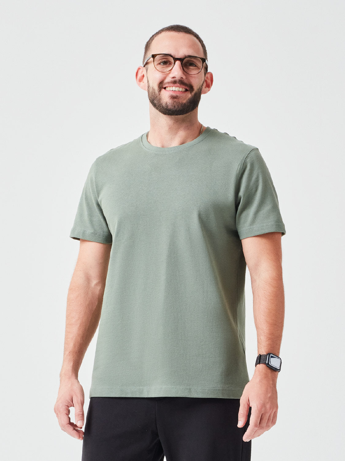 Ein Mann mit Brille der ein Premium TShirt in der Farbe Grün aus Bio-Baumwolle trägt, dazu hat er eine passende schwarze Hose an - nachhaltige Mode für einen lässigen Look.