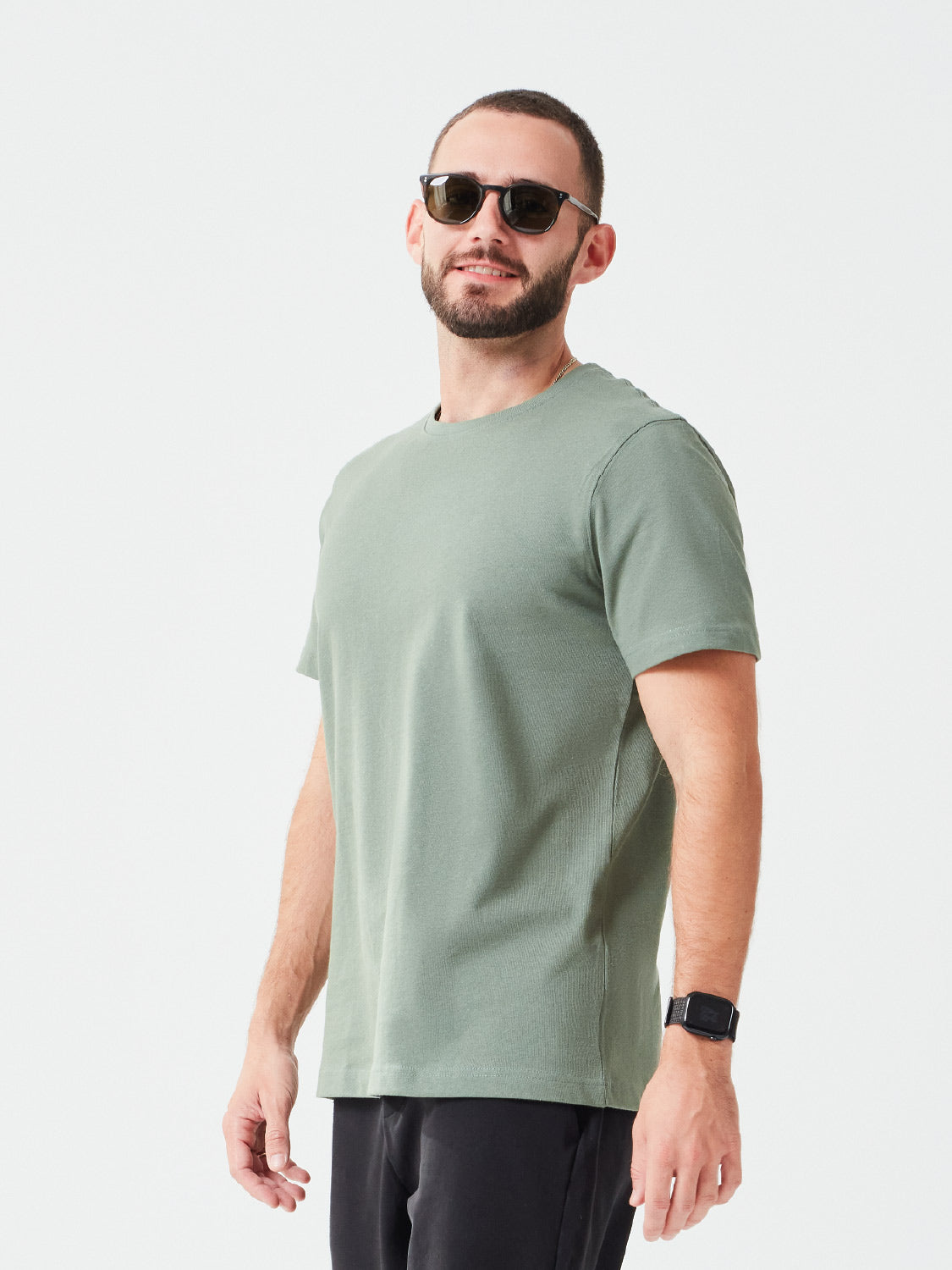 Ein Mann der ein Premium TShirt in der Farbe Grün aus Bio-Baumwolle trägt, dazu trägt er eine Sonnenbrille und er hat eine passende schwarze Hose - nachhaltige Mode für einen lässigen Look.
