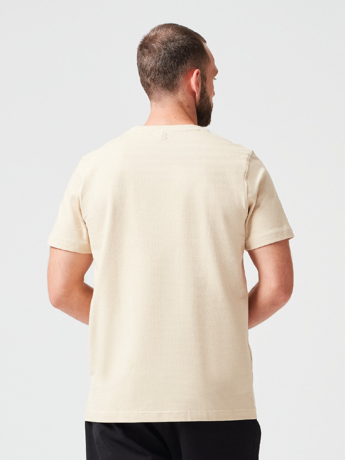 Rückansicht eines Mannes der ein Premium TShirt in der Farbe Sand aus Bio-Baumwolle trägt - nachhaltige Mode für einen lässigen Look.